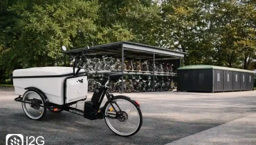 Triporteur vélo cargo blanc stationné devant un parc vélos à étages et des consignes fermées, solution de mobilité douce professionnelle I2G.