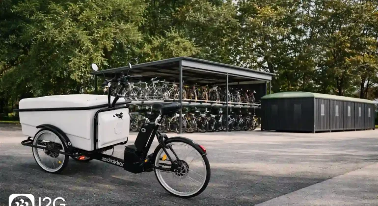 Triporteur vélo cargo blanc stationné devant un parc vélos à étages et des consignes fermées, solution de mobilité douce professionnelle I2G.